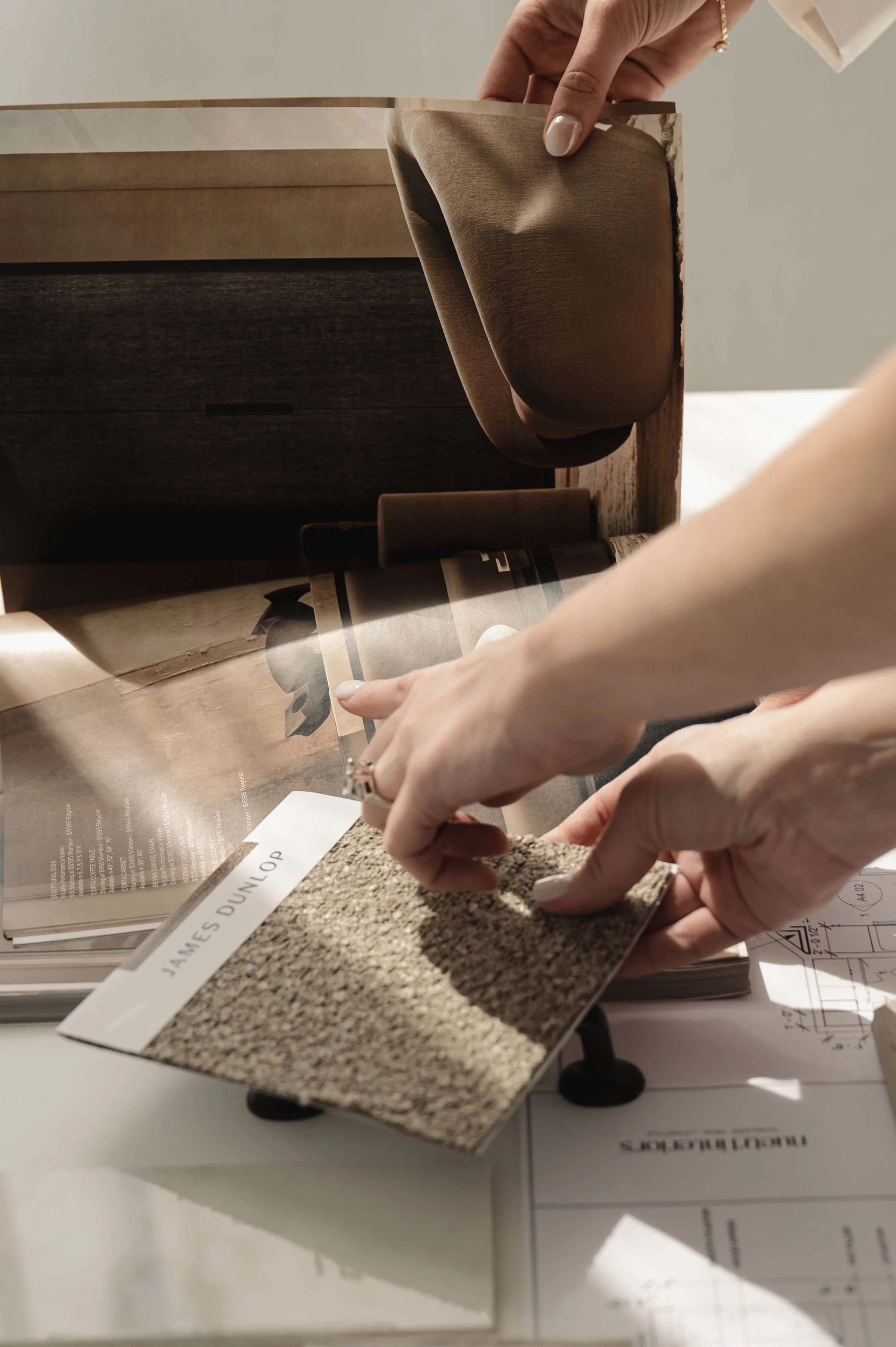 Person holding a paint sample card labeled James Dunlop, inspecting fabric, with swatches and sample books on a table.