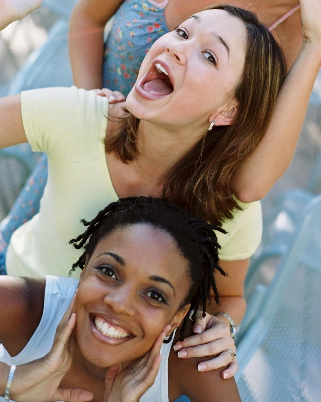 Two women smiling and having fun, one holding the other's head, and both looking joyful.