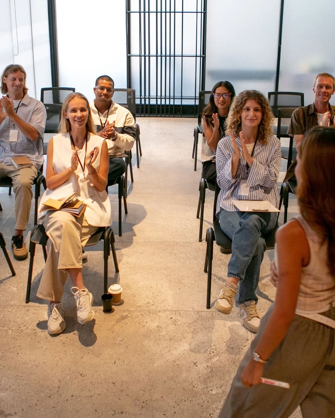 People sitting and clapping at a conference or seminar in a modern glass-walled room.