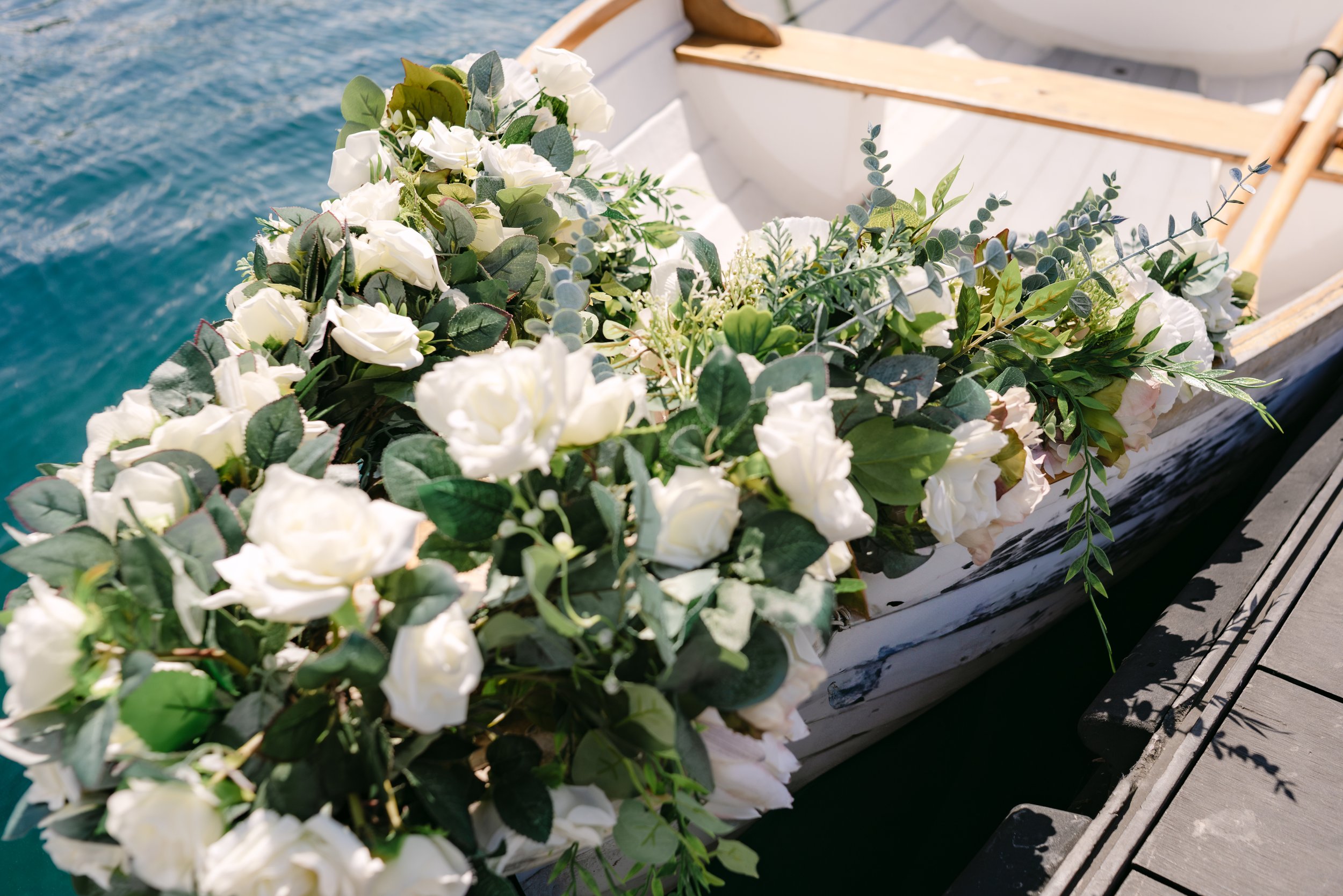A boat decorated with white and green floral arrangements, floating on water near a wooden dock.