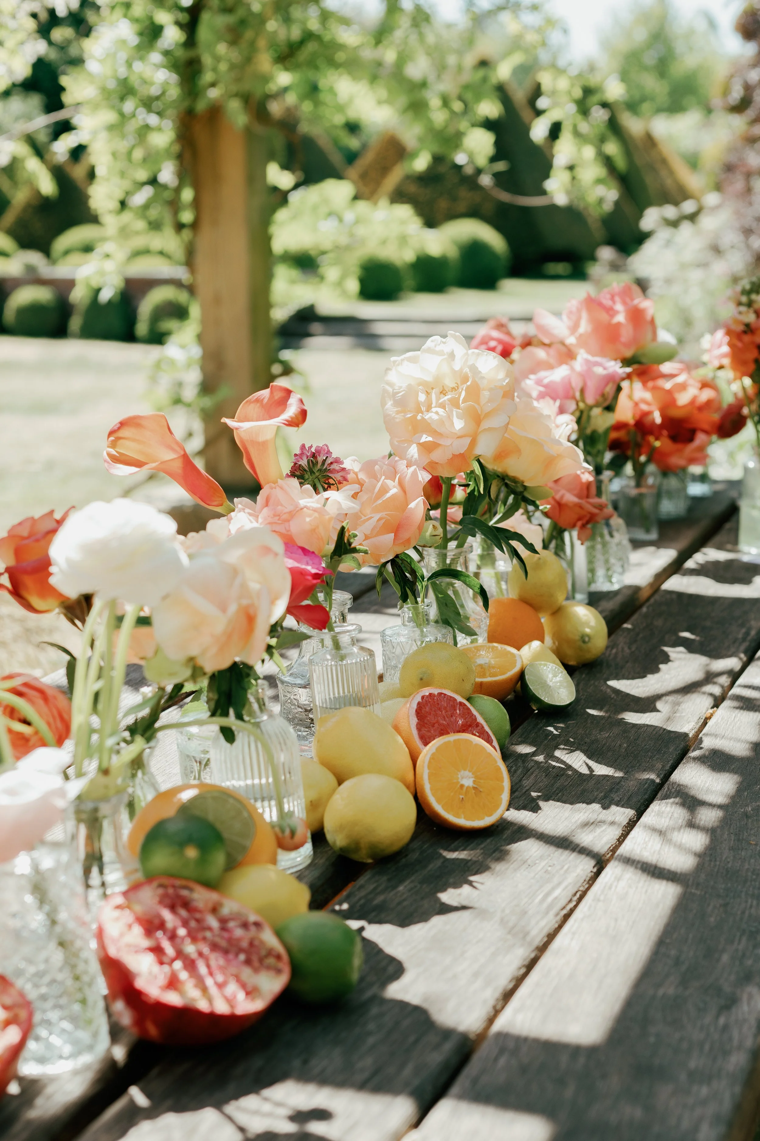 Colorful flowers and assorted citrus fruits arranged on a wooden table outdoors