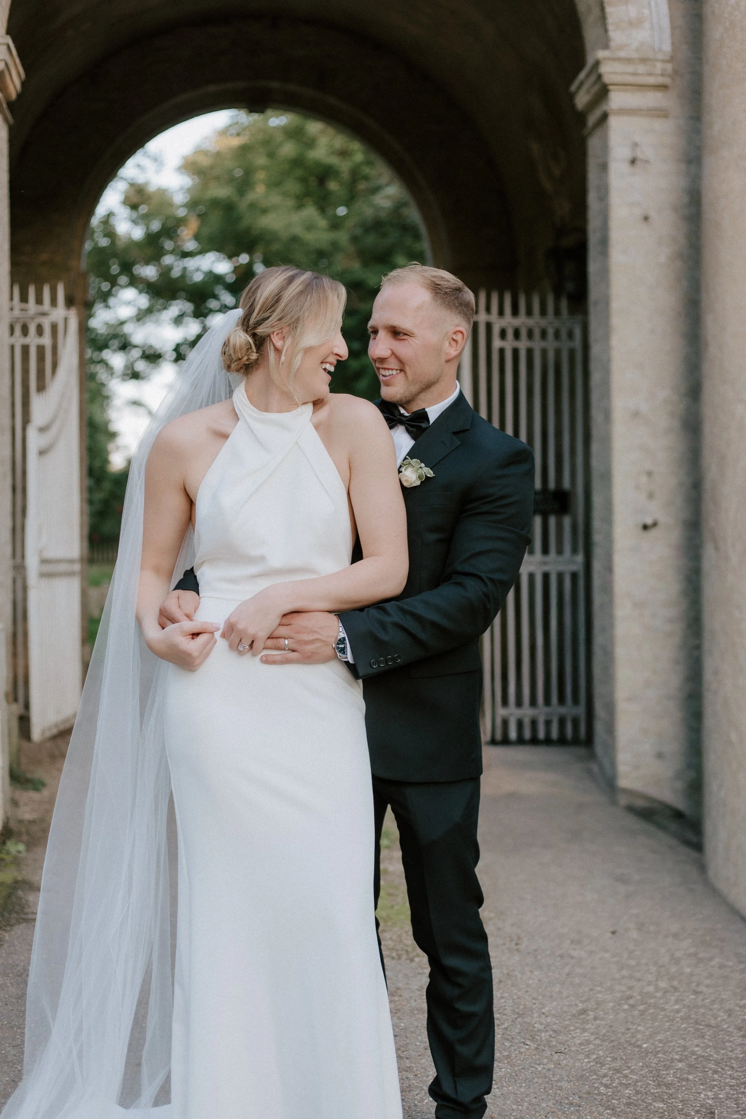 Romantic and elegant wedding photographer Suffolk and Norfolk – bride and groom sharing happy moment in front of arched gate.