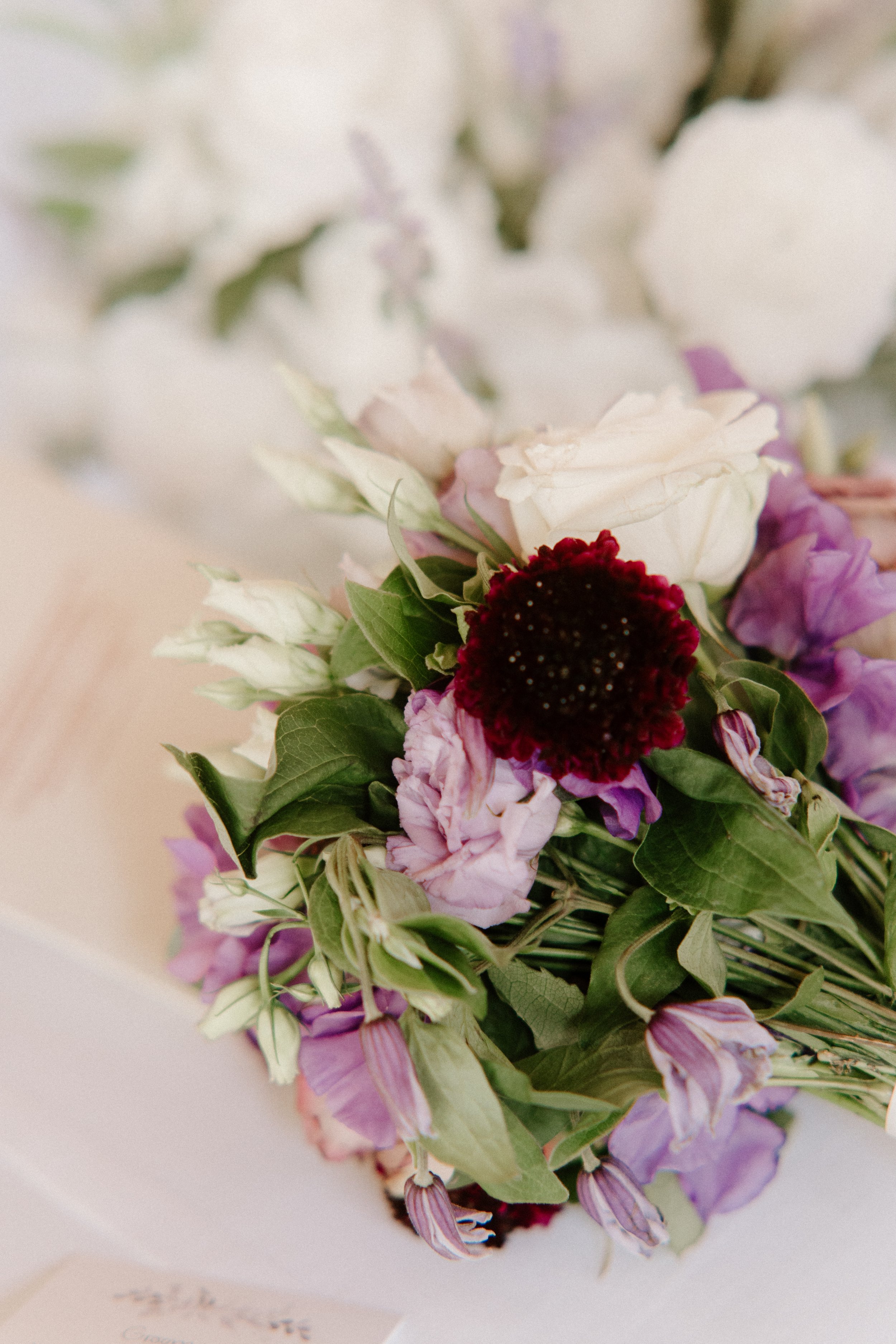 Close-up of a colorful floral bouquet with white, purple, and dark red flowers and green leaves.