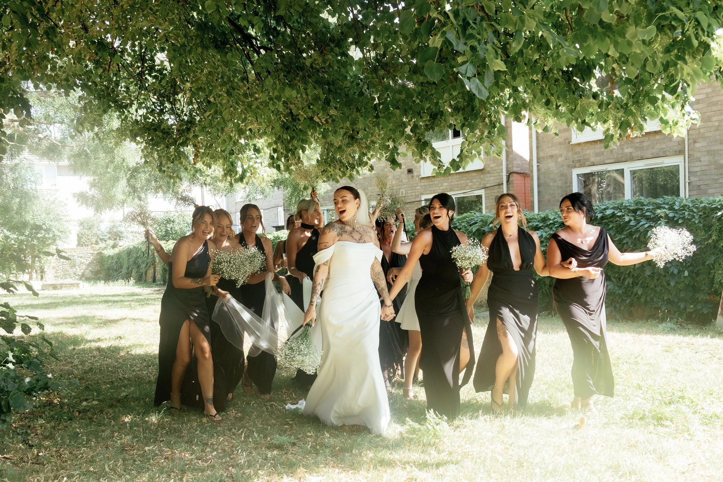 Bridal party laughing in sunlight and shadows – emotional wedding moments captured by Suffolk documentary wedding photographer.