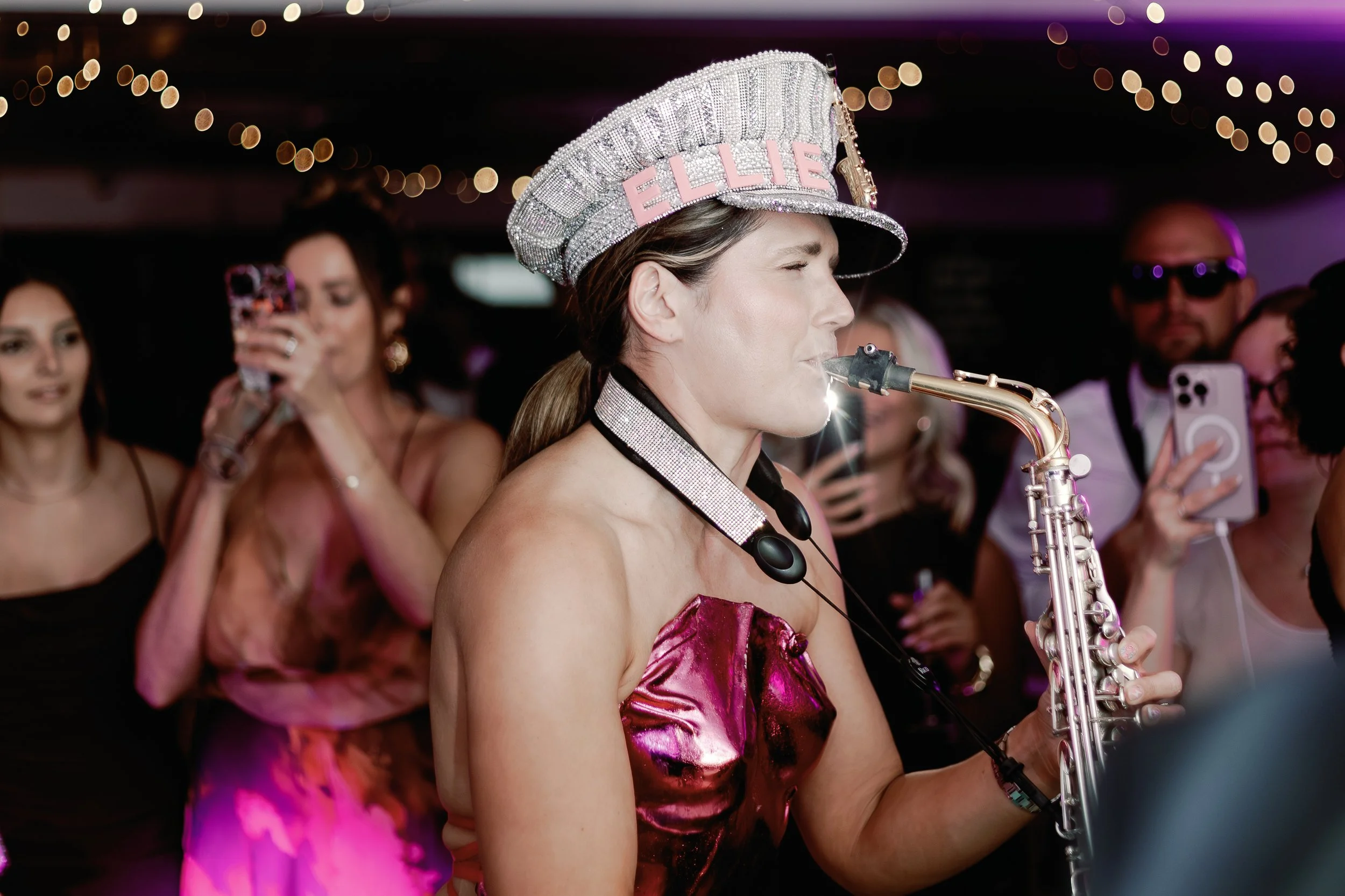 Live saxophonist Elllie Sax performing on the dance floor at a stylish Suffolk wedding, surrounded by guests capturing the moment — perfect for couples seeking unforgettable wedding entertainment and vibrant photography.