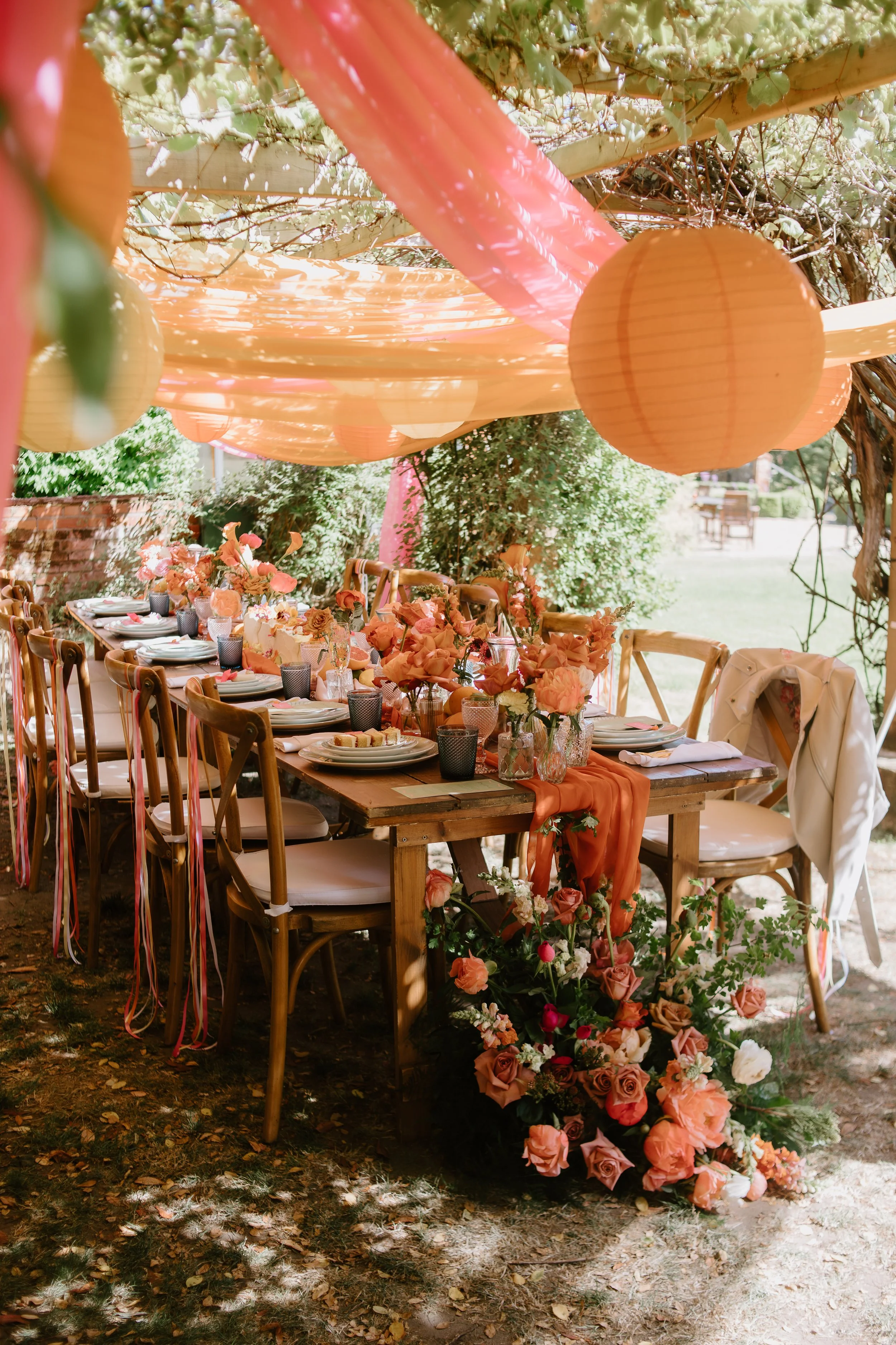 Decorated outdoor dining table with flowers, candles, and pastel-colored balloons and fabric for a celebration or party.