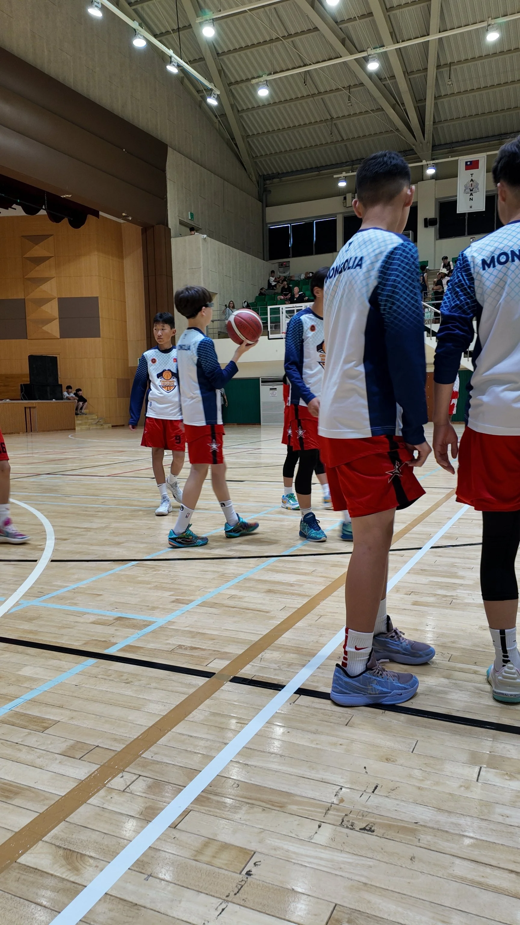 Young basketball players in blue and white jerseys and red shorts practicing on indoor basketball court.