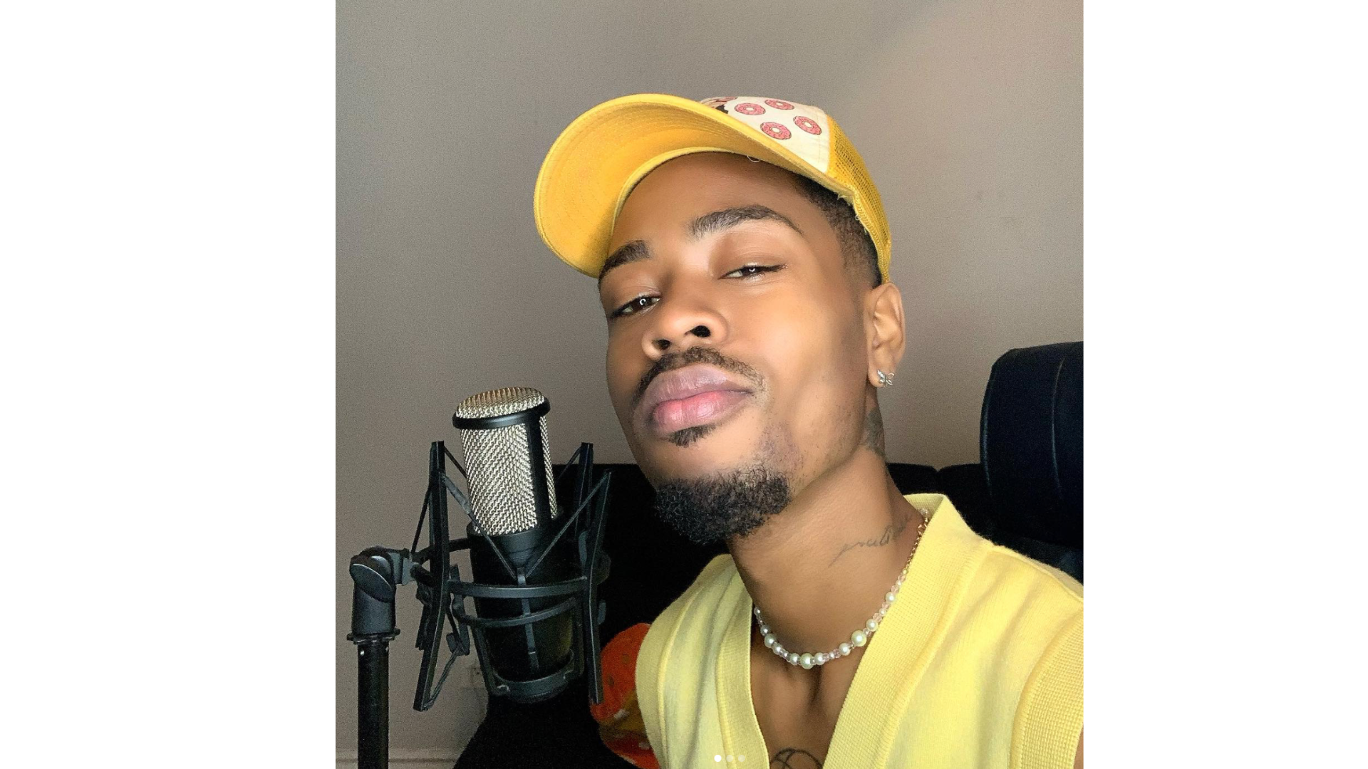 Bryyce singer-songwriter Person wearing a yellow cap with a pearl necklace in front of a microphone indoors.