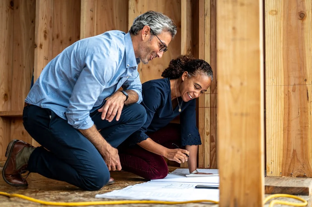 A man and woman inspecting blueprints inside a wooden framing structure.