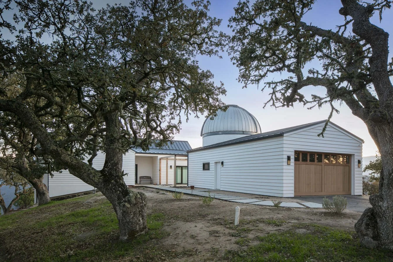 A white house with an observatory dome, surrounded by trees, with a cloudy sky in the background.