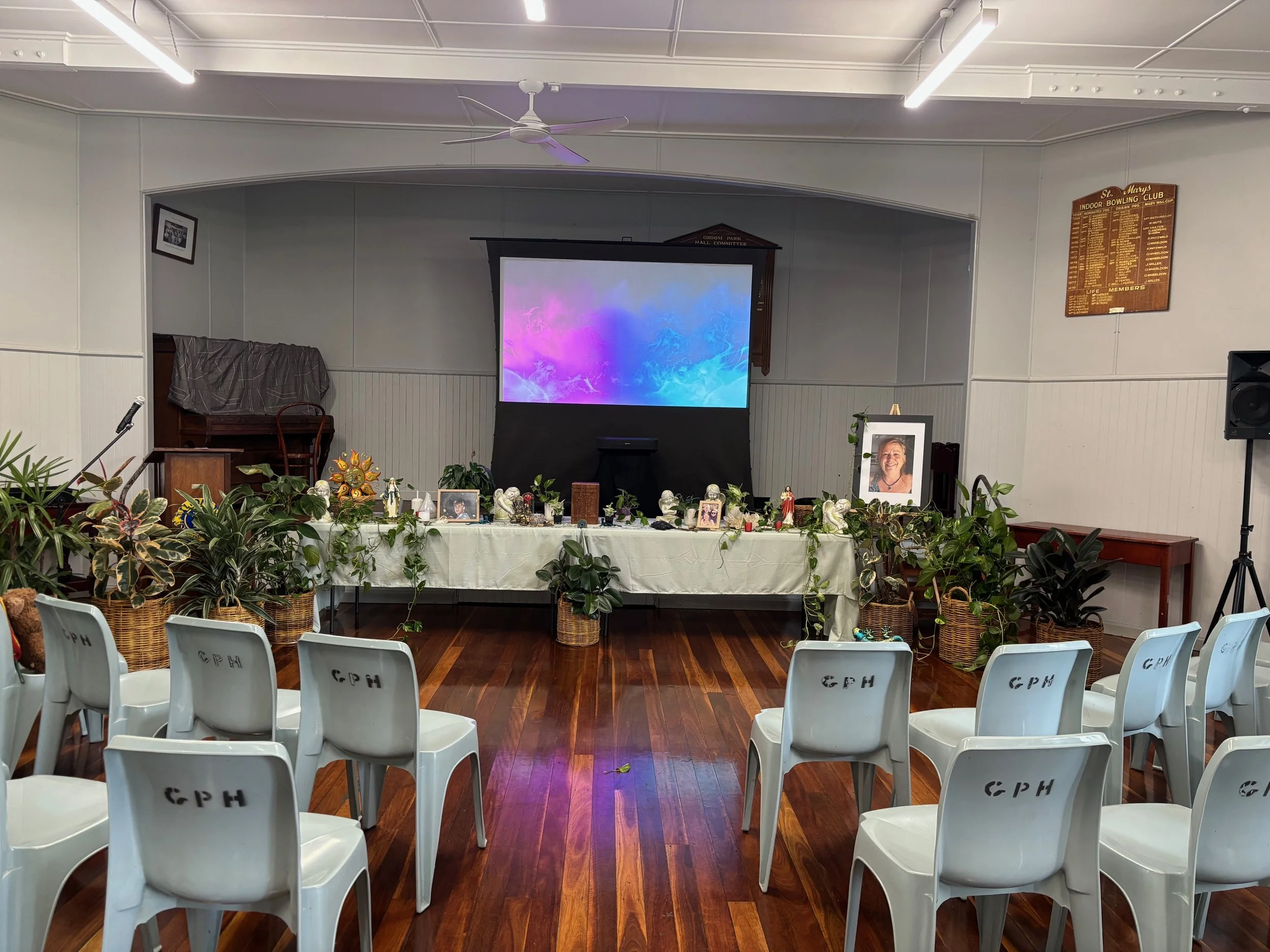 A memorial service held in a community hall, where the deceased dedicated her life to helping others. The funeral team built an alter out of the deceased's belongings, and instead of buying flowers, plants were hired to honour her love of her garden.
