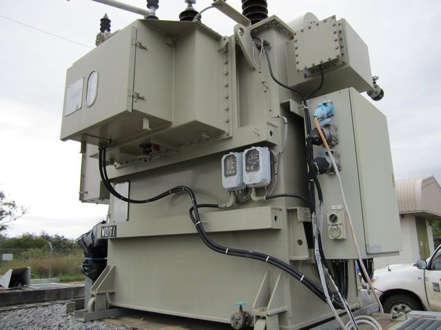Industrial electrical transformer with cables and connectors, installed outdoors on a concrete platform.