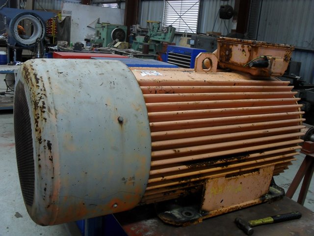 Large industrial electric motor in a workshop with various tools and machinery in the background.
