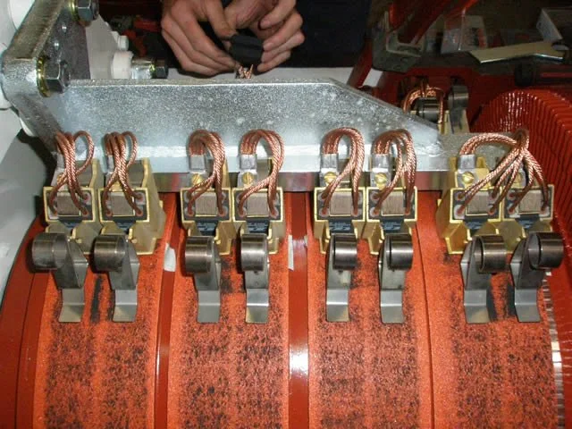 Close-up view of electrical components including copper wires, connectors, and a metallic frame, with a person's hands visible at the top, adjusting the components.