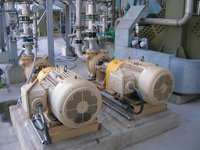 Industrial pumps and motors in a factory setting, with connected pipes and valves, on concrete platforms.