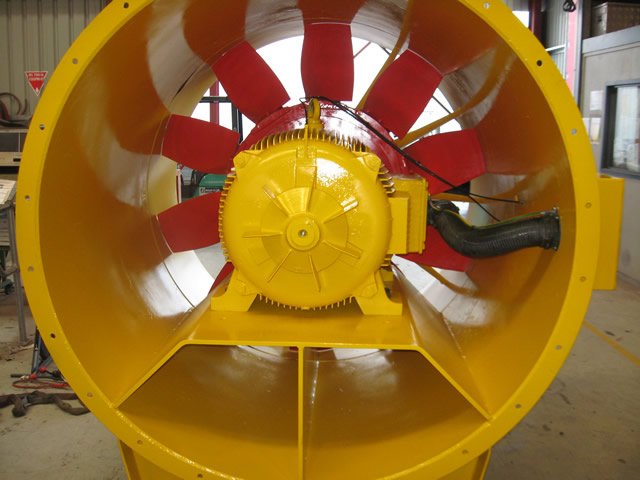 Large industrial axial fan with yellow housing and red blades inside a factory setting.