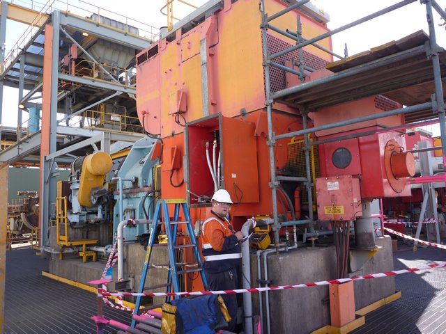 Industrial site with large machinery and a worker inspecting equipment