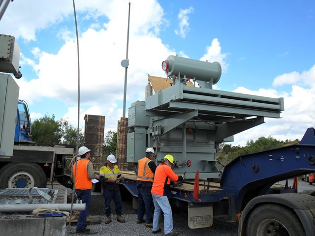 Workers in safety gear standing beside a large industrial machine on a flatbed truck.