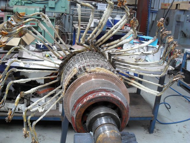 Industrial motor with damaged winding coils in a workshop setting.
