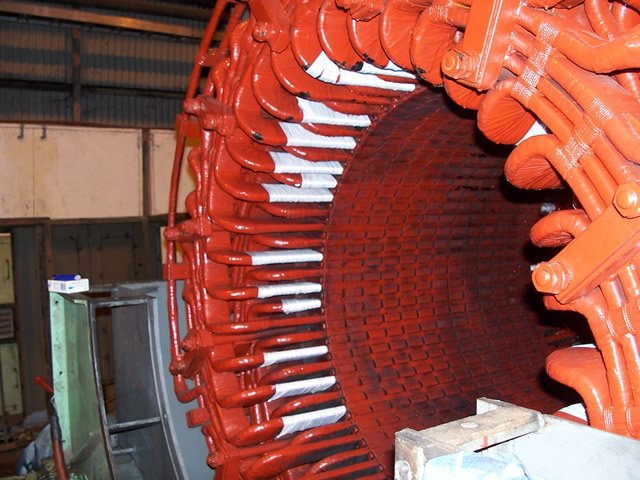 Close-up of a large red electrical stator coil winding in an industrial space.