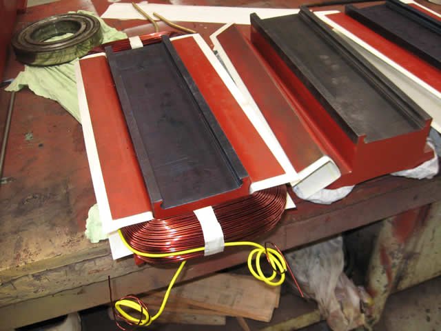 Industrial components on a workbench, including red metal parts and copper wire coils.