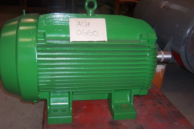 Green industrial electric motor with label "ACH 0660" on top, mounted on a red surface in a workshop setting.