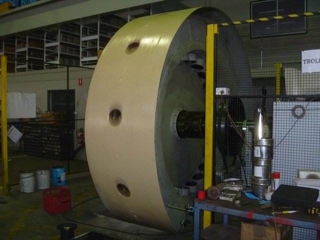 Large industrial flywheel in a workshop setting with tools and equipment around it.