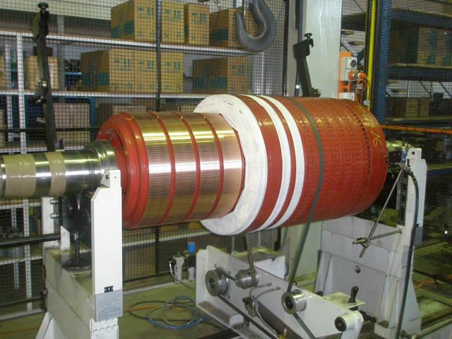 Industrial machine rollers with red and white materials wound around the central shaft, situated in a manufacturing facility.