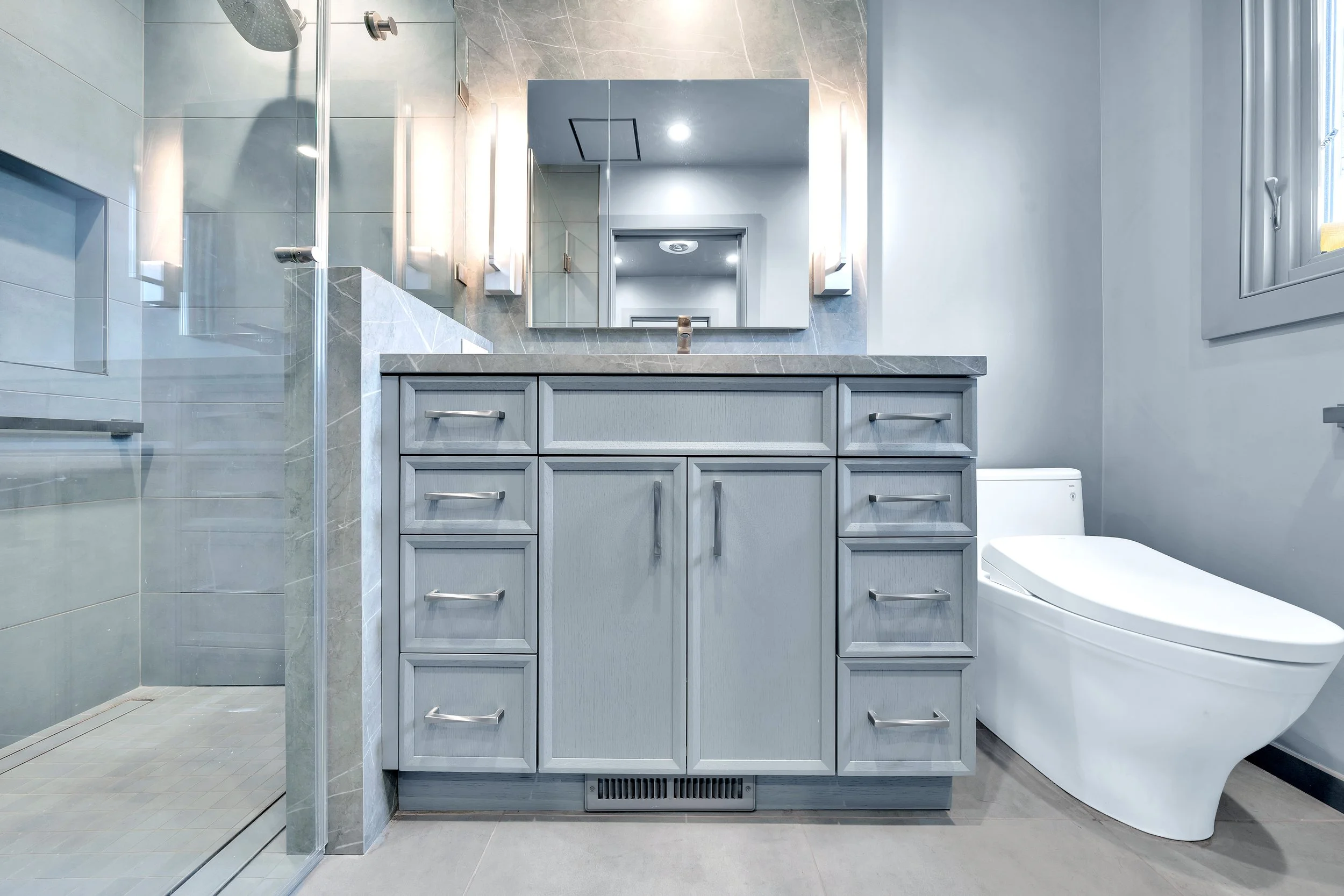 Modern bathroom with a gray vanity, large mirror, toilet, and walk-in glass shower.