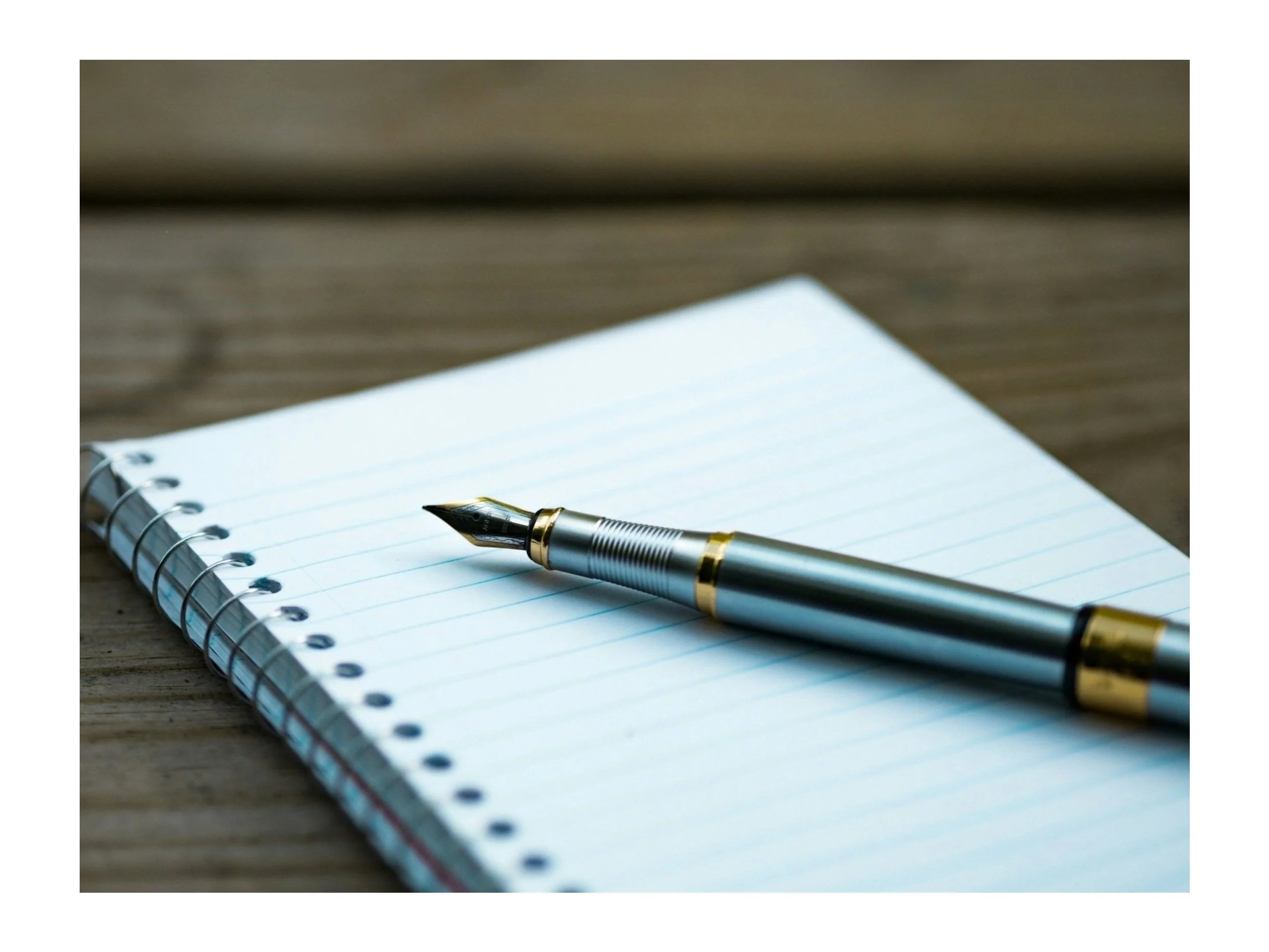 Fountain pen resting on an open spiral notebook with lined paper on a wooden table.