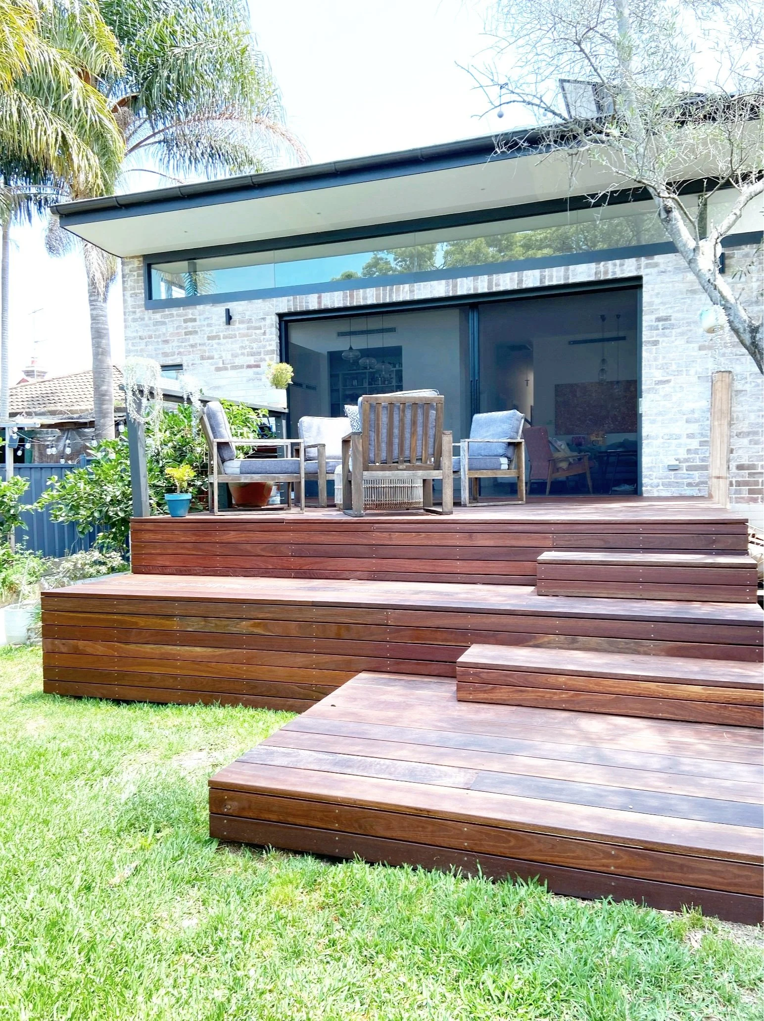Backyard wooden deck with outdoor furniture and sliding glass doors, brick house exterior, trees, and green grass.