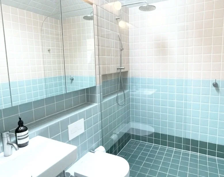 Bathroom with light blue and cream square tiled walls and floor, shower area with a rain showerhead, mirror, sink with soap dispenser, and toilet.