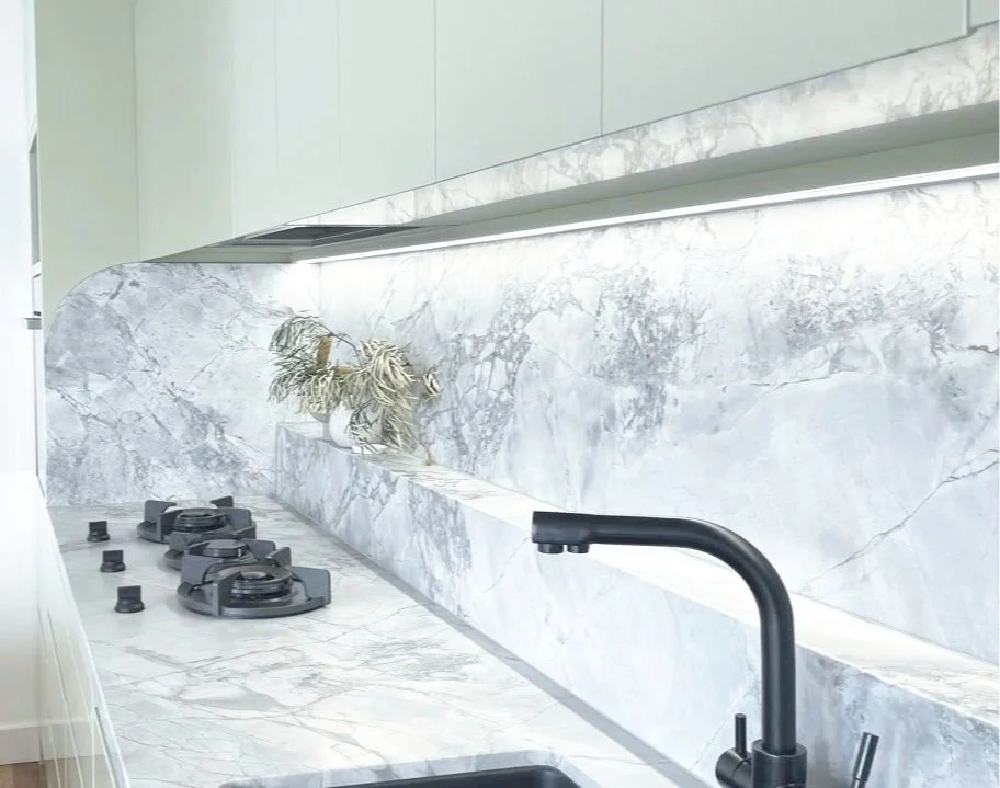 Modern kitchen countertop with marble surface, black gas stove burners, a black faucet, and a decorative plant. The backsplash is made of matching marble.