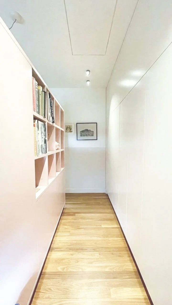 Hallway with wooden floor, pink custom storage and bookshelves on the left, white walls, framed picture, and ceiling with recessed lighting