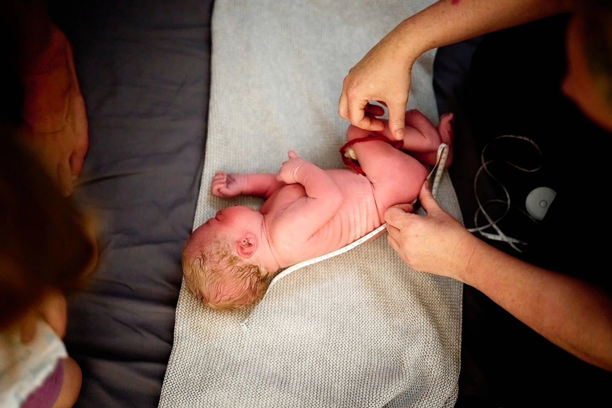 A newborn baby on a padded surface during a medical examination, with a healthcare professional measuring the baby's length.