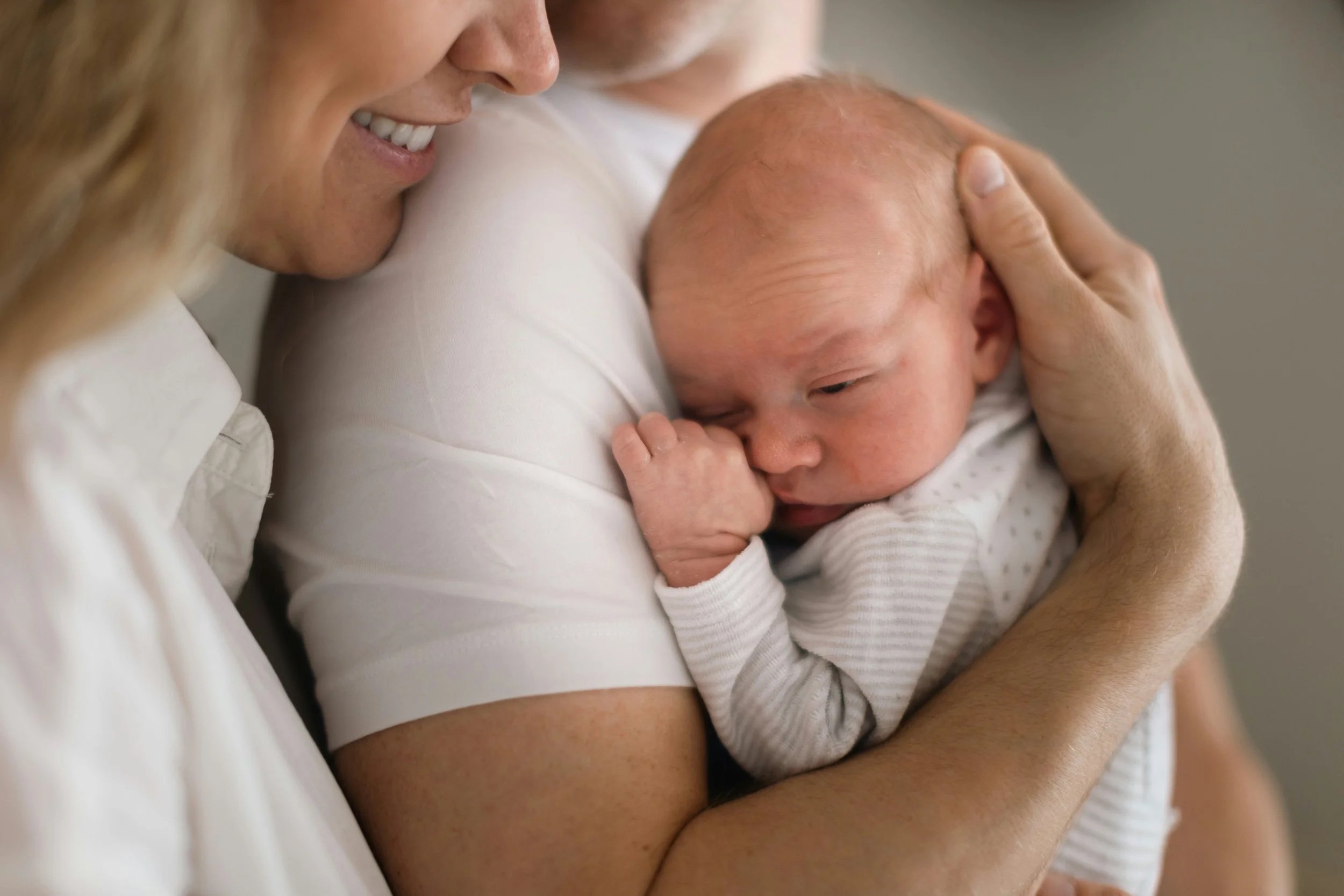 Parent cradling a sleeping newborn against their chest, hands gently supporting the baby