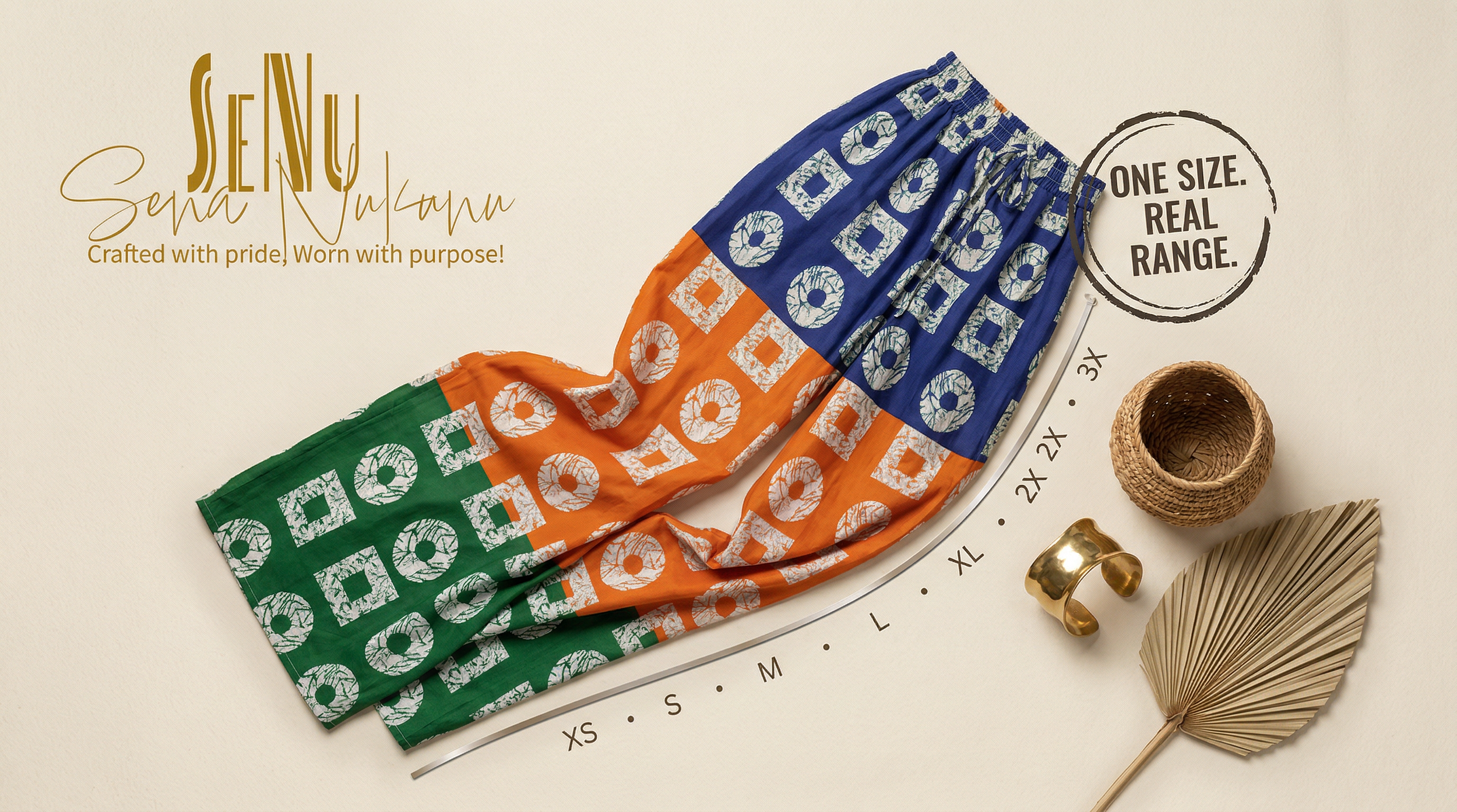 Colorful fabric pants with geometric pattern in green, orange, and blue laid out on a surface, surrounded by decorative objects including a gold ring, a gold cuff bracelet, a woven basket, a gold palm leaf, and text indicating size range from XS to 3X, with an overlay message 'One size. Real range.'