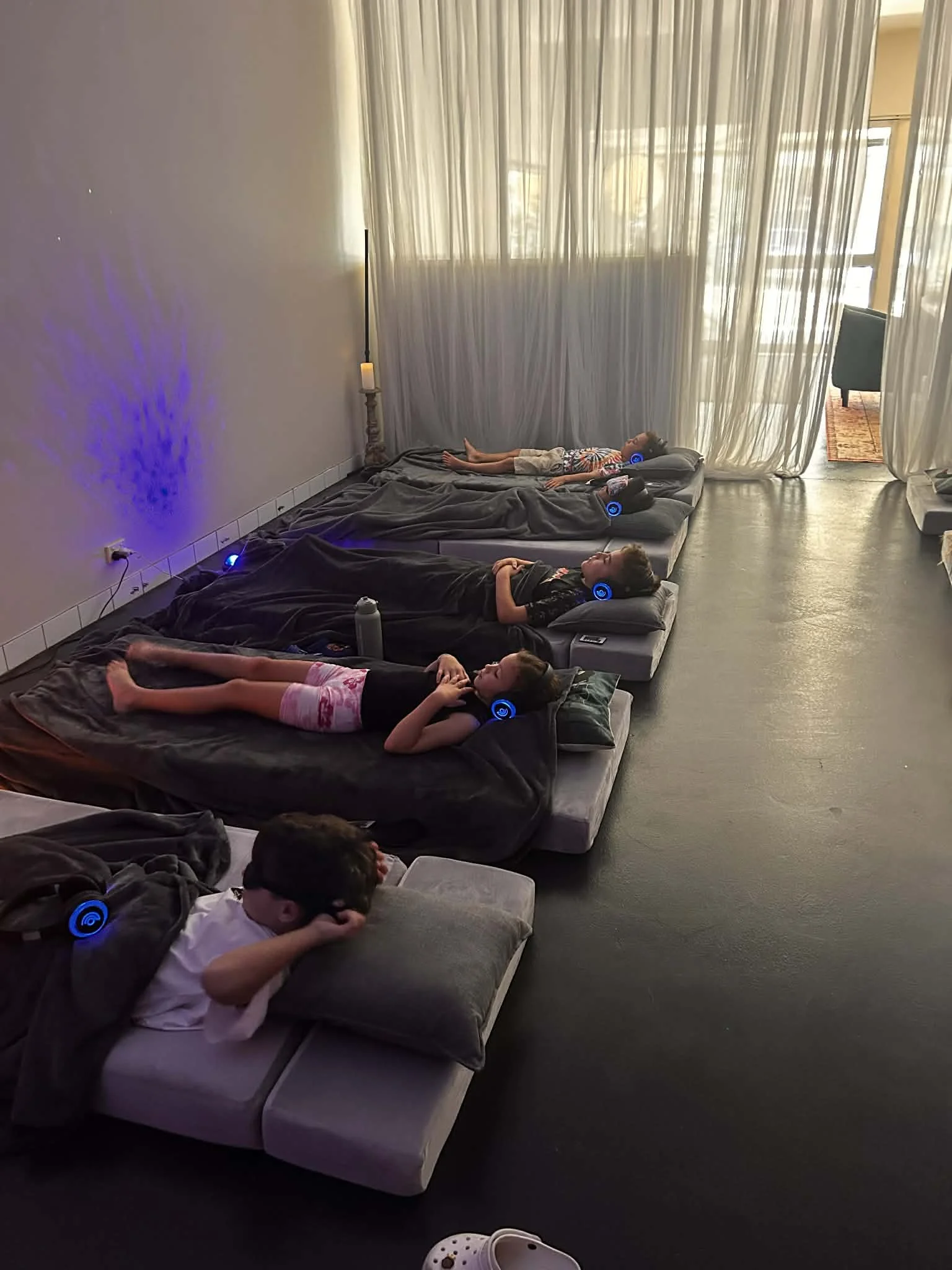 Children lying on mats with headphones during a kids breathwork session at Kora Wellness Port Kembla, with purple ambient lighting