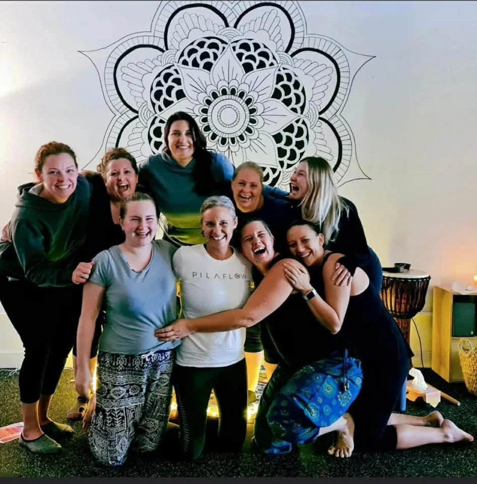 Hayley Simpson with a group of women after her first breathwork session, laughing together in front of a mandala mural