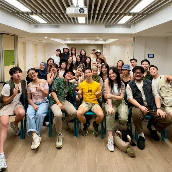 Group of young people smiling and posing for a photo in a room with a projector on the ceiling.