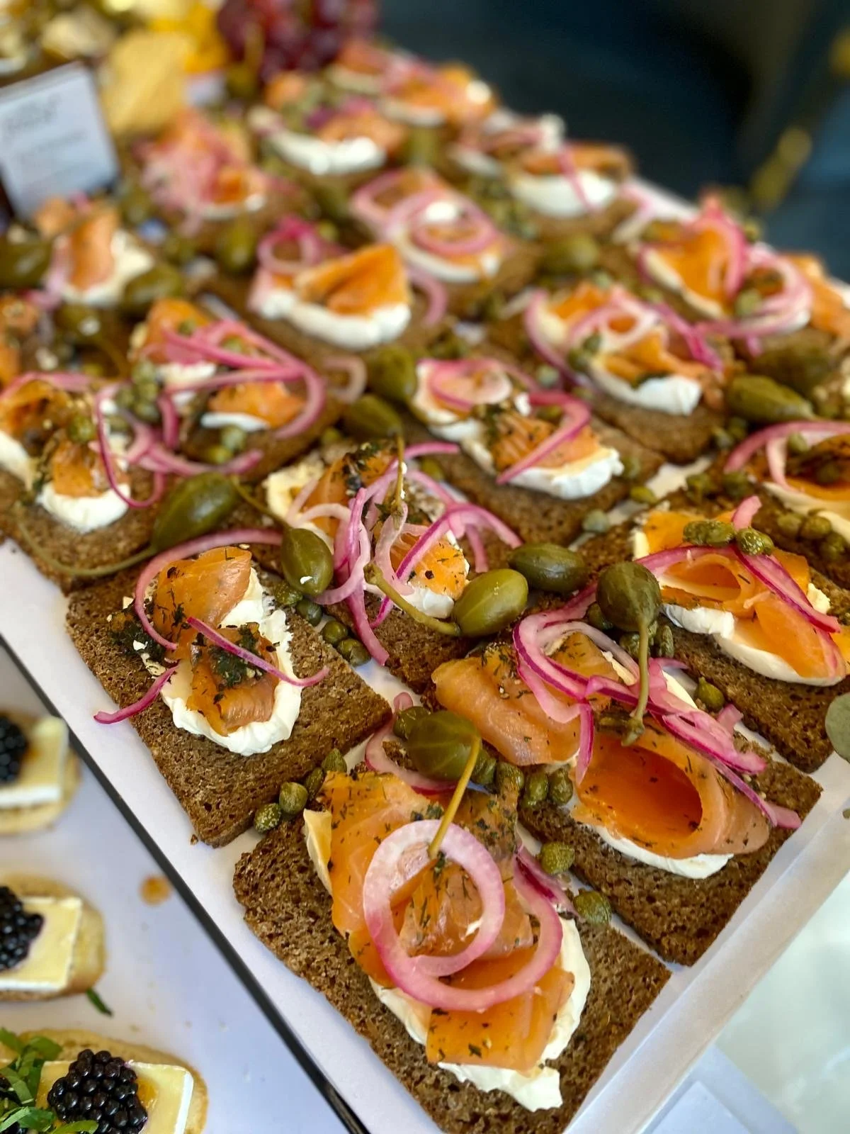Open-faced smoked salmon canapés with cream cheese, pickled onions, capers, and herbs on rye bread.