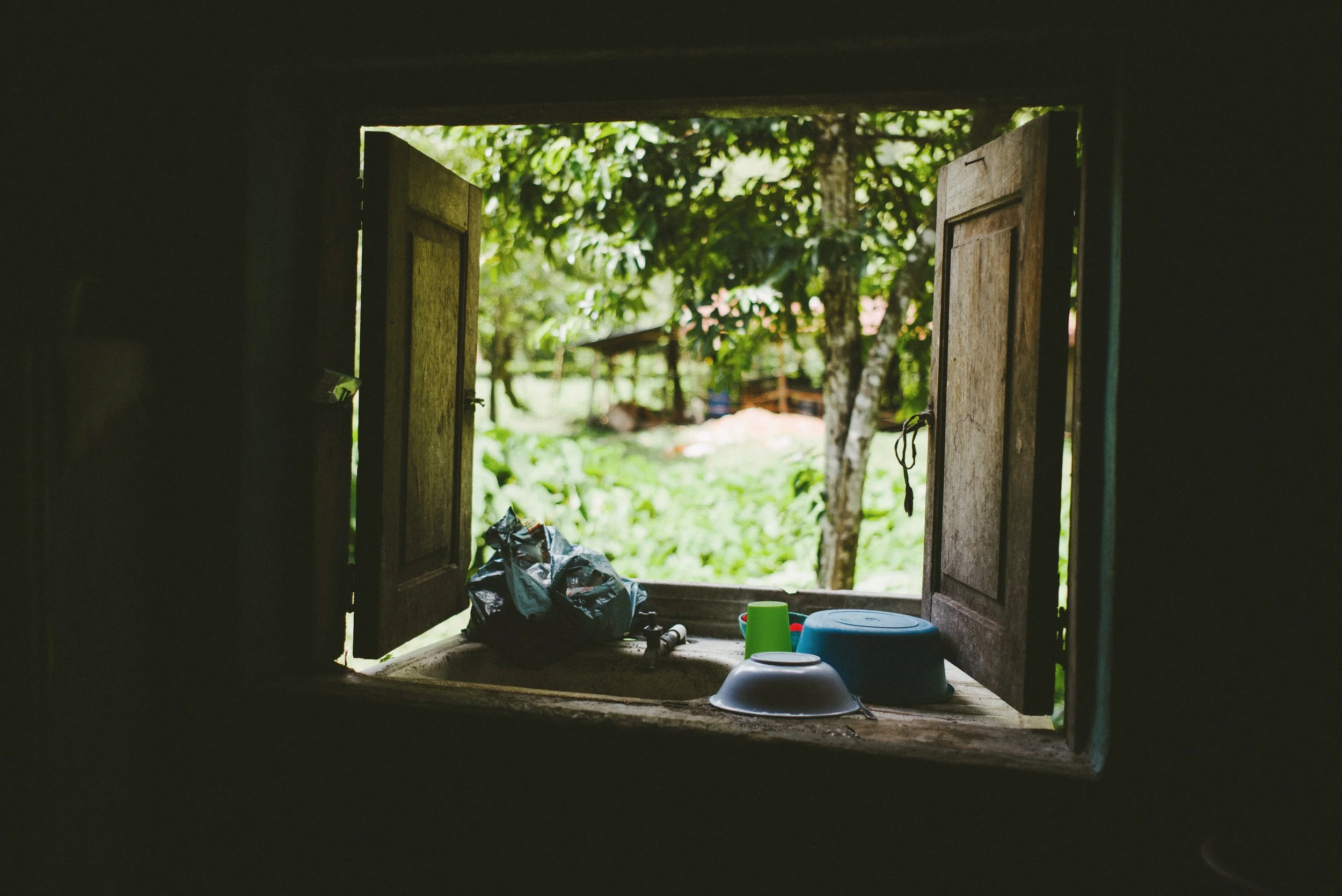 Open wooden window with dishes on the ledge and a view of greenery outside