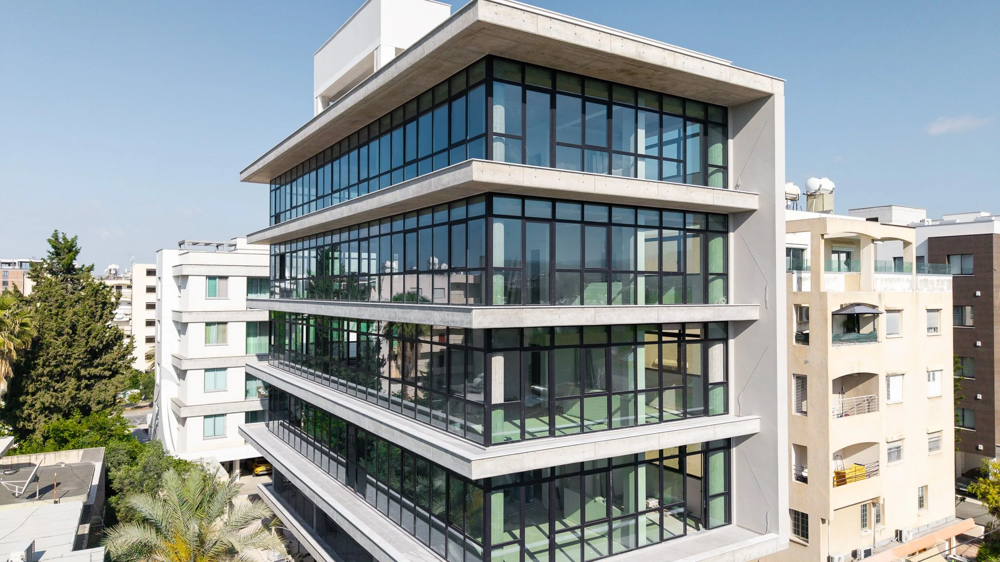 Modern multi-story office building with glass exterior, trees, and parked cars in front.