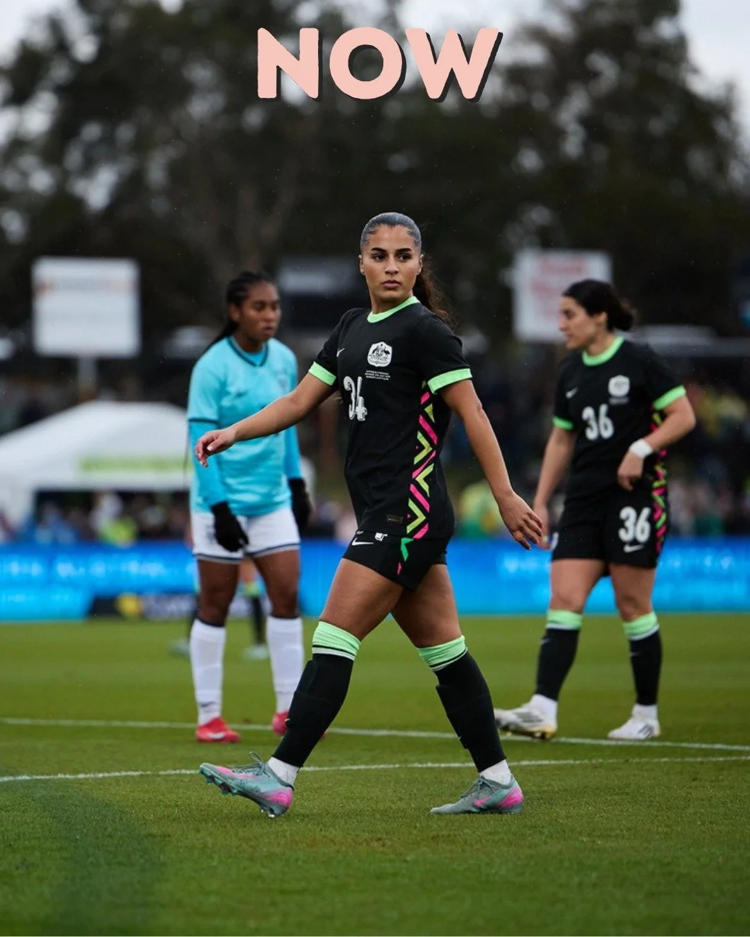 A women's soccer match showing three players in black and one player in blue on a grass field, with the word 'NOW' in pink above.