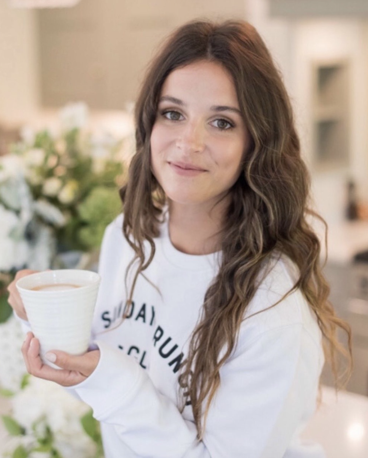 A person with a neutral expression wearing a black tank top, standing against a textured brick wall.