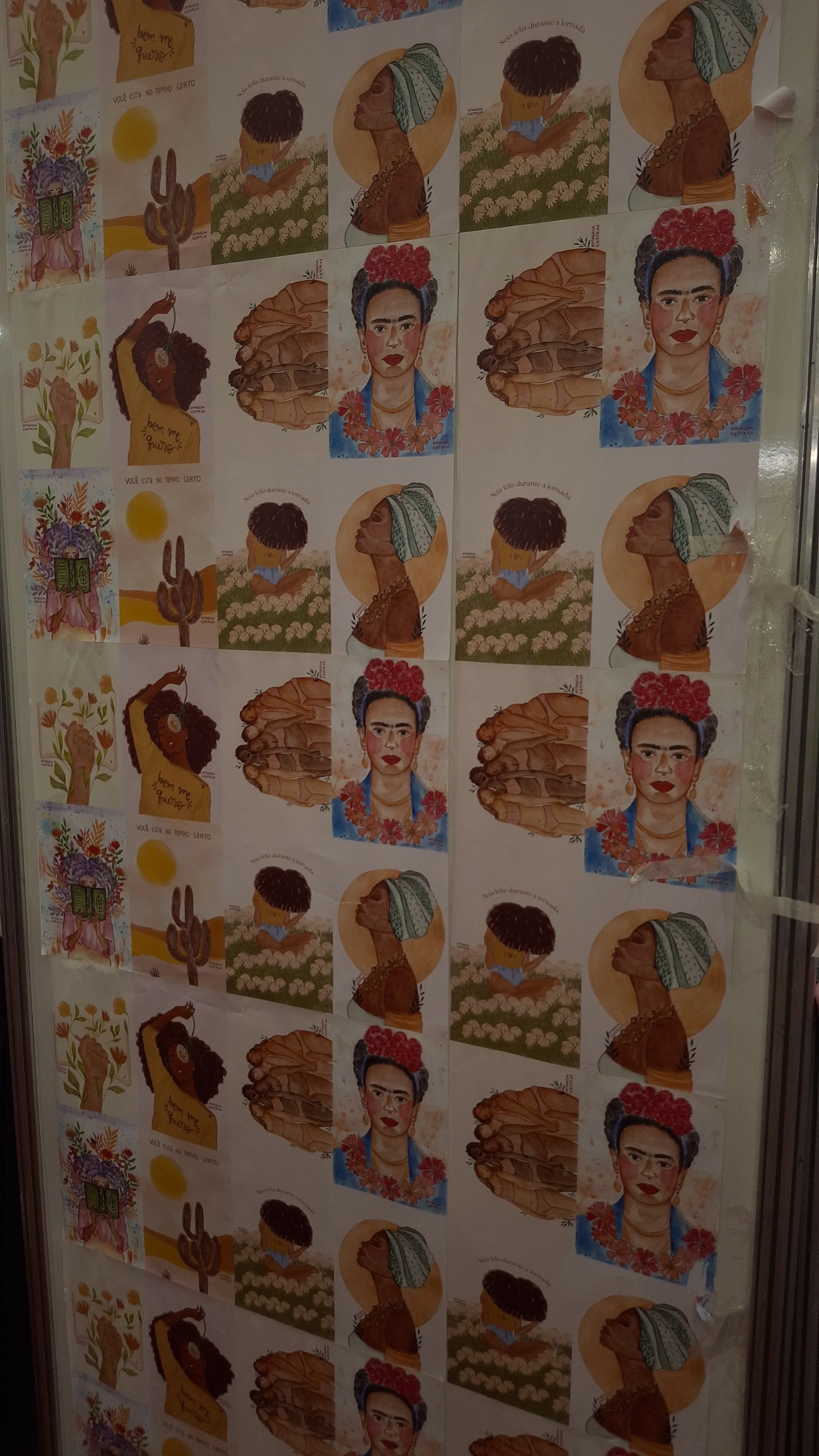 A wall covered with multiple printed illustrations of women in traditional Mexican attire, flowers, and landscape scenes, arranged in a grid pattern.