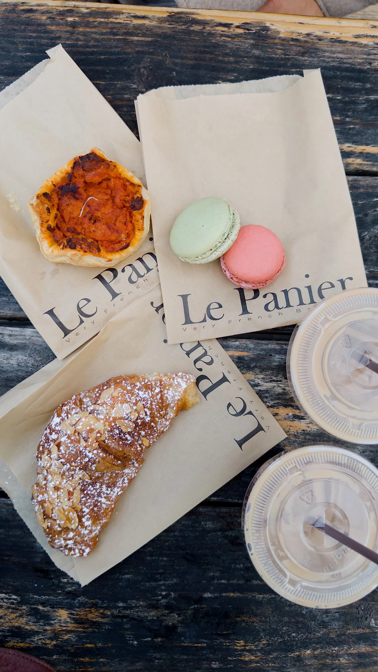 Sweet pastries and macarons on parchment paper with drinks on a wooden table.