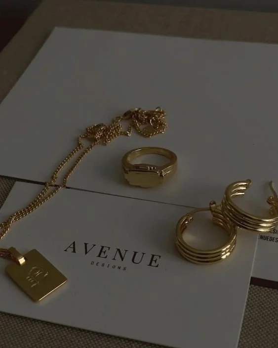 Gold necklace, rings, and earrings displayed on a white paper with 'AVENUE DESIGNS' printed on it.