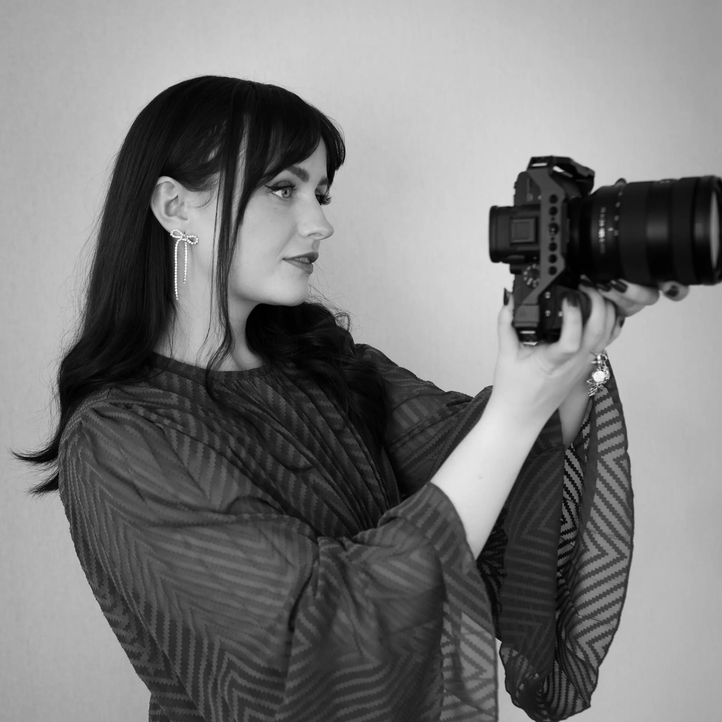 Black and white photo of a woman with dark hair and earrings aiming a camera.