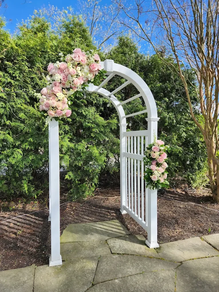 A breathtaking, hand-tailored pink and white roses wedding arch installation by Quogue Flower Shop, the premier choice for luxury Hamptons estate weddings and coastal ceremony design.